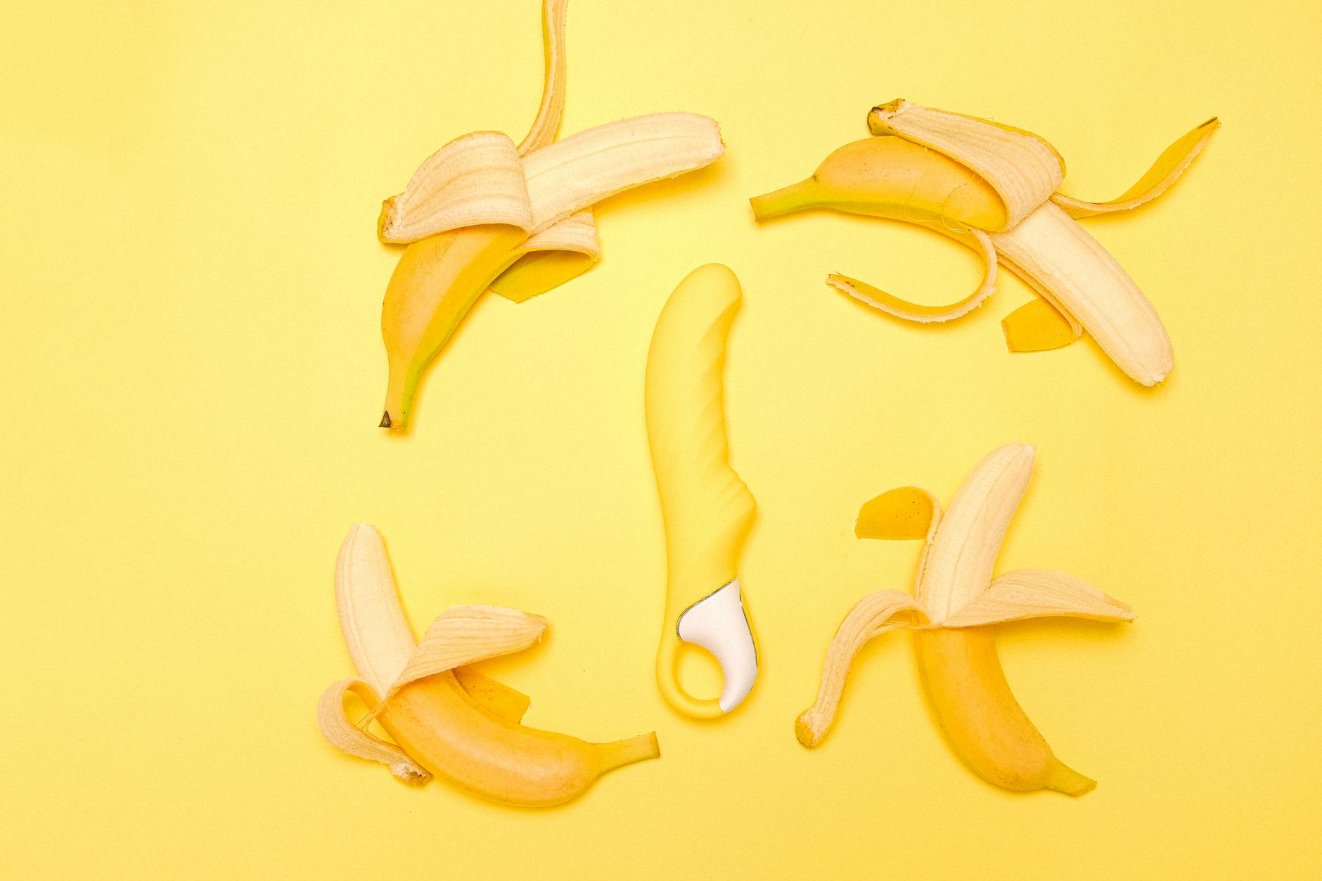 Yellow silicone clitoral vibrator surrounded by peeled lemons on a bright yellow background