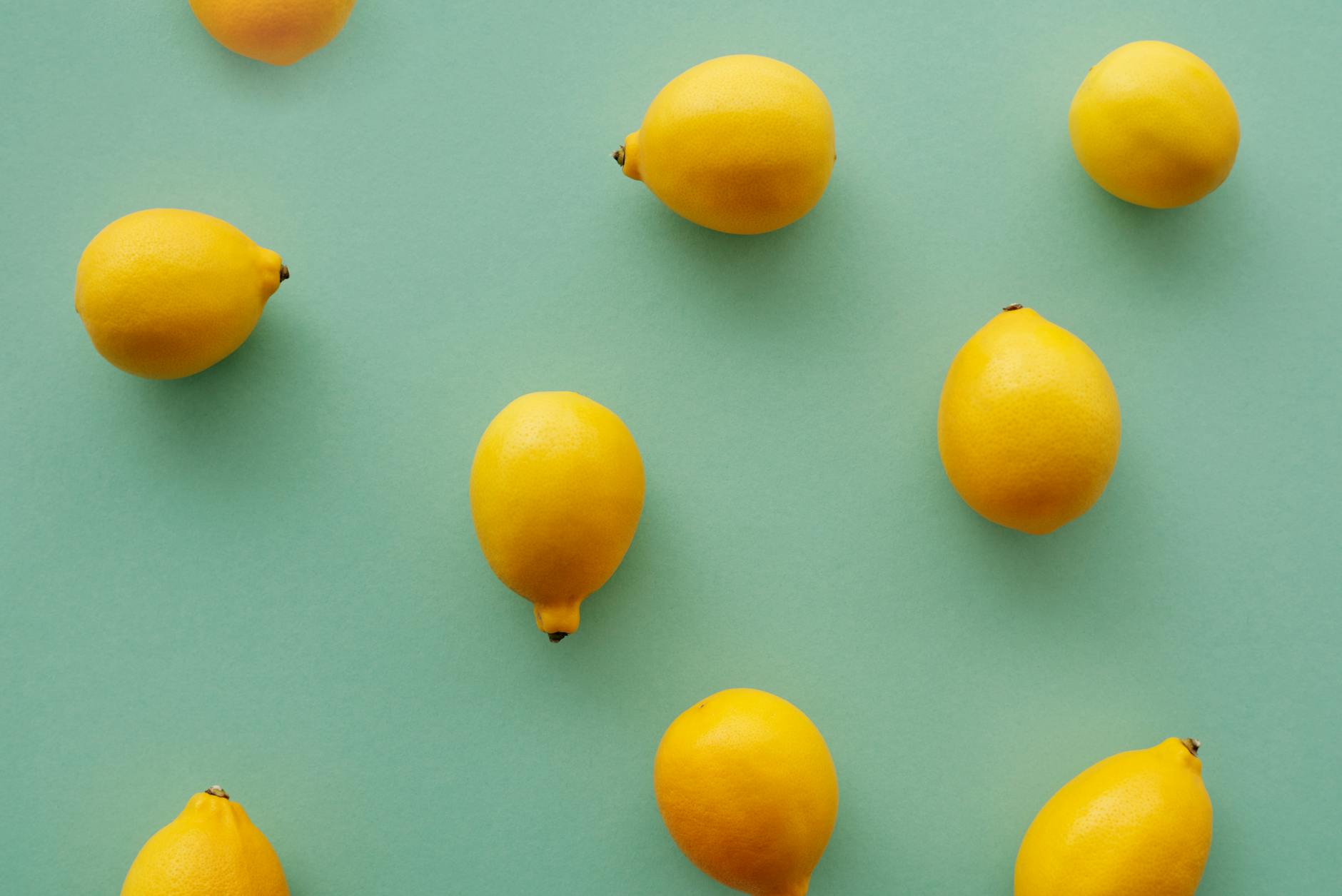 Bright yellow lemons arranged on a pastel green background, symbolizing freshness and wellness