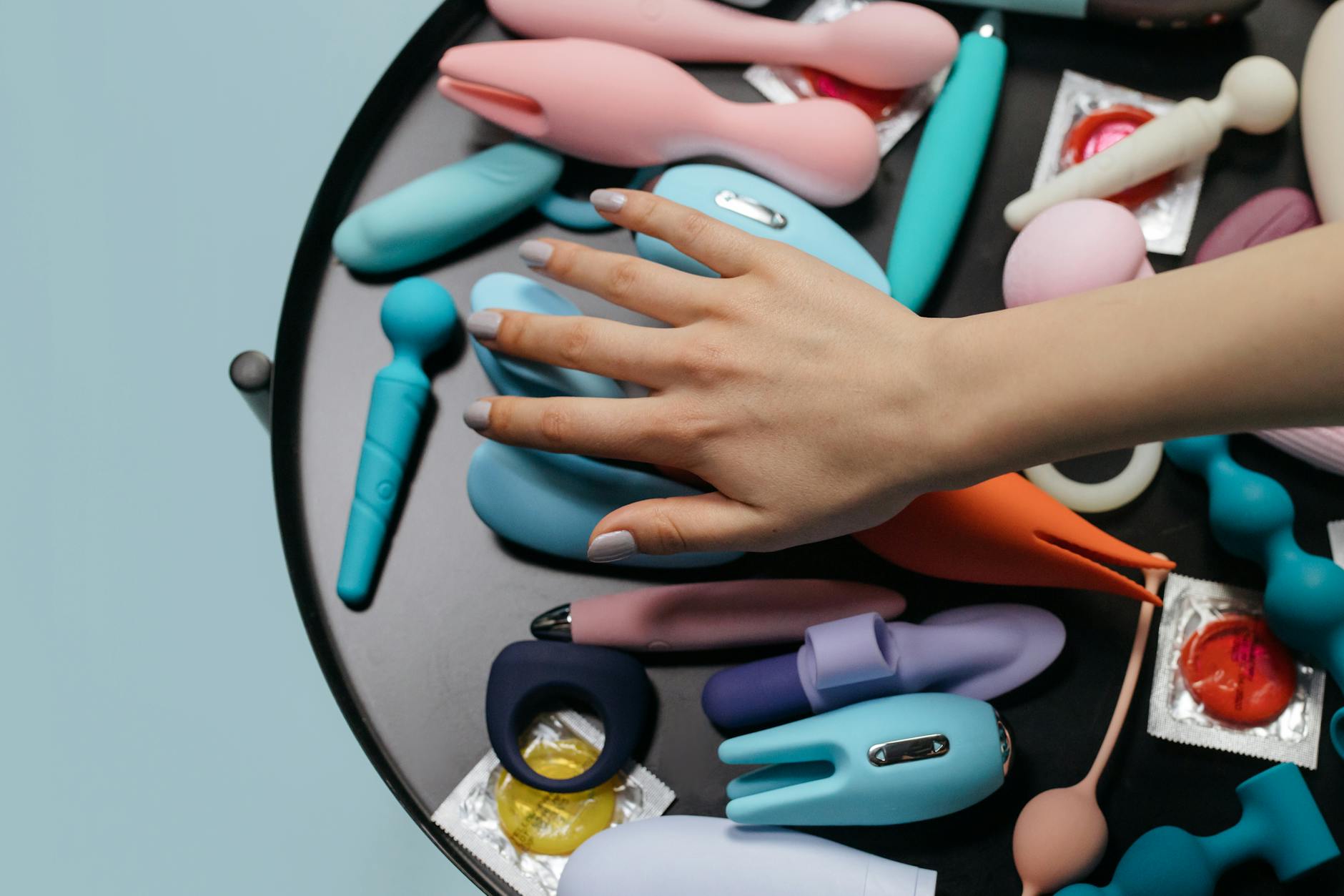 Woman holding blue and pink vibrators in a thoughtful pose
