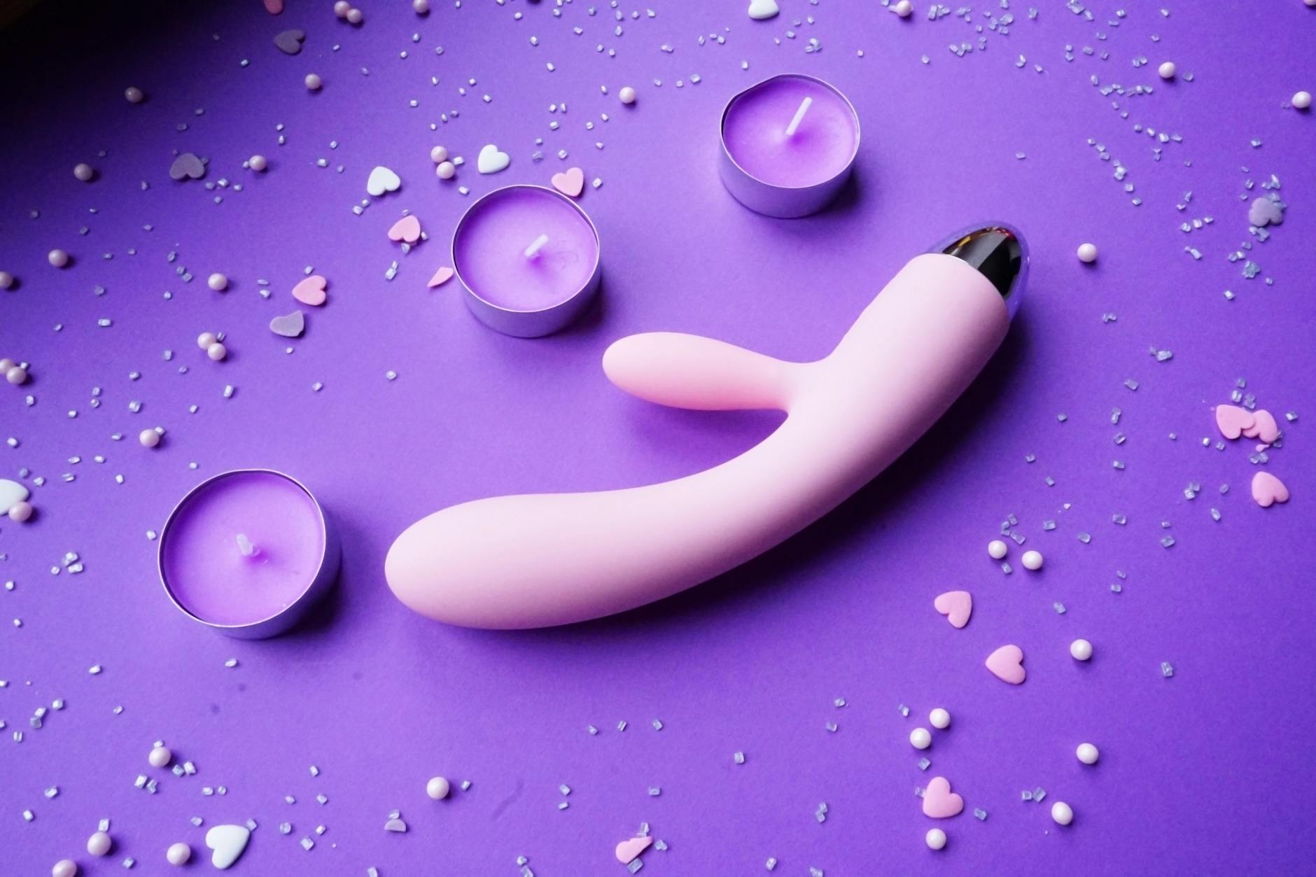 Rangée de stimulateurs vibrants colorés arrangés sur une surface rose avec des confettis en forme de cœur